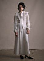 Front facing image of a long sleeved silk mid length dress with a self fabric bow at the neck in ivory. 