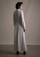 A back-facing image of a model wearing an ivory long sleeved silk mid length dress. 