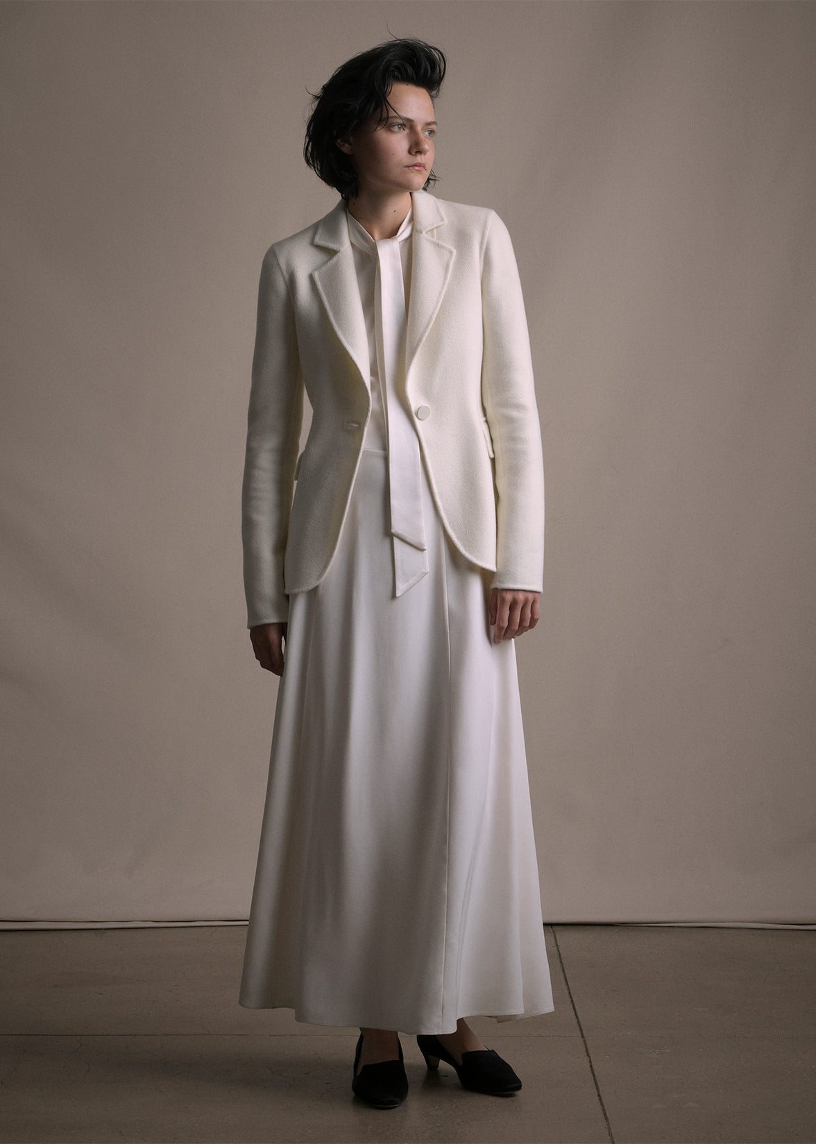 Image of a model wearing an ivory cashmere blazer layered over an ivory silk dress by Adam Lippes