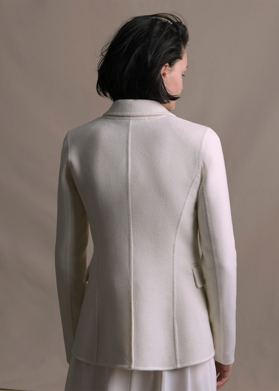 Image of a model turned backwards wearing an ivory cashmere blazer by Adam Lippes