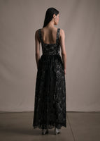 Model facing backward wearing a black lace long sleeveless dress.