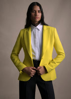 Image of a model from the waist up wearing a yellow single button blazer over white button down shirt, with black pants.