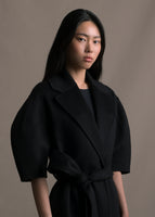 A zoomed in image of model wearing a long black regency coat with short balloon sleeves and a front waist tie.