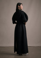 A back-facing image of a model wearing a long black regency coat with short balloon sleeves.