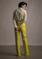 A back-facing image of a model wearing a white and citrine long sleeve shirt with collar and thin bow in stripe shirting with citrine pants.