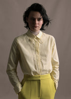 Model wearing a white and citrine long sleeve shirt with collar and thin bow in stripe shirting with citrine pants.