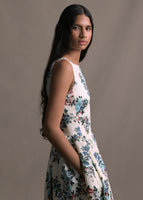 A model wearing a sleeveless white floral dress, image from the hips up.