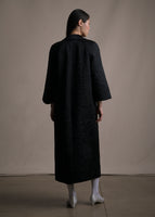 A back-facing image of a model wearing a long black quilted opera coat.