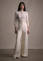 Image of a model standing forwards wearing an ivory cashmere cardigan tucked into ivory wide leg pants.