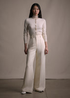 Image of a model standing forwards wearing an ivory cashmere cardigan tucked into ivory wide leg pants.