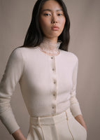 Model wearing a black long sleeve cashmere cardigan with small crystal buttons on the front. Lace top under the sweater. 