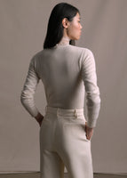 A back-facing image of a model wearing a white long sleeve cashmere cardigan and ivory pants. 