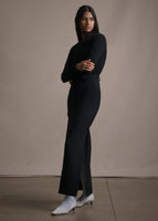 Side angle shot of model wearing a black sweater with long black pencil skirt.
