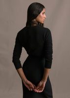 A back-facing shot of a model wearing a black cashmere cardigan paired with a black skirt
