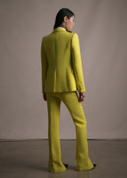 A back-facing image of a model wearing a long citrine pair of pants with a matching blazer. 