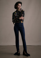 Model facing forwards wearing black floral button down shirt tucked into navy neoprene flare pants.