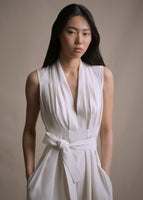 Close up image from the waist up of a model wearing a white V-neck sleeveless jumpsuit. 