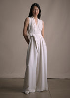 Image of a model facing forwards wearing an ivory sleeveless v-neck jumpsuit with a fabric belt at the waist.