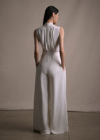 Image of a model standing backwards wearing an ivory silk jumpsuit with her hands in her pockets.