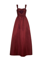Flat lay of a floor length fit and flare merlot gown in duchess satin with thin straps and gathered bow-like front torso.