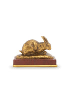 A bronze model of a crouching rabbit with its ears up on a red stone base.