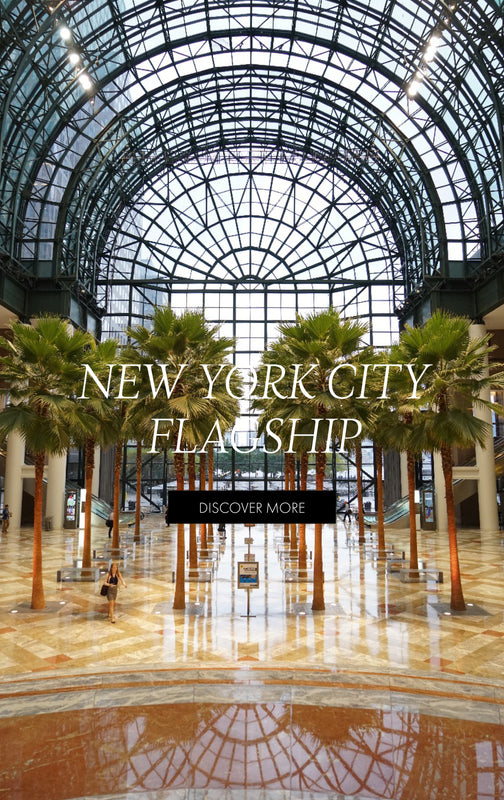 New York City flagship. Discover More. An image of the inside of a building with a glass rotunda ceiling and palm trees.