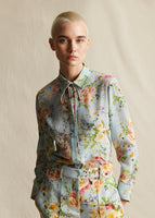 A close-up from waist up, of a model wearing a pale blue floral silk long sleeved top and matching pants.