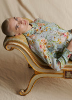 A model laying on a vintage chaise wearing a light blue floral long sleeved shirt.