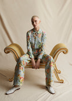 Model sitting on a vintage stool wearing a pale blue floral wide leg pant, with a matching pale blue floral long sleeved shirt.