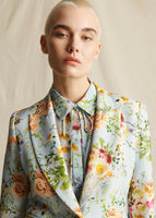 A close-up image of a model wearing a pale blue floral printed blazer, with matching collared shirt.