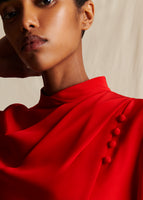 A close-up of a model wearing a red mock neck draped dress with 4 small fabric covered buttons
