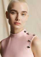 Close up image of a model wearing a light pink mock neck dress with 5 gunmetal buttons near neckline.