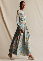 Model standing sideways wearing a pale blue floral, long sleeved, maxi dress.
