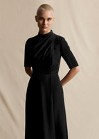 A closer image from knees up of a model wearing a black short sleeved dress.