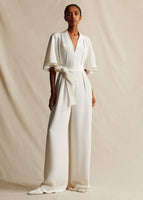 A model standing straight forward wearing ivory silk full length jumpsuit with sleeves and a waist belt.