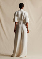 Image of a model facing backwards wearing an ivory silk sleeved jumpsuit. 
