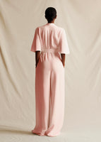 A model standing backwards wearing a short sleeved light pink jumpsuit.
