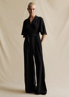 A model wearing a short sleeved black jumpsuit with fabric belt at the waist.