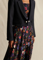 Close-up image of a cropped black blazer with pearl buttons at the center front, styled over a floral pleated dress.