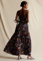 Model standing backwards wearing a black floral pleated long sleeveless dress.