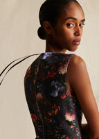 Close-up of a model from the waist up wearing sleeveless black floral dress, with a grosgrain tie on the zipper.