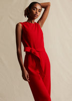 A model wearing a red sleeveless jumpsuit with a fabric belt tied around the waist.