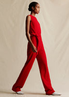A model wearing a red sleeveless jumpsuit with a fabric belt at the waist.
