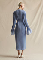 A model standing backwards wearing a light blue pleated midi dress with flounce cuff and self tie at waist.