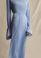 A close-up image a model wearing light blue pleated midi dress with flounce cuff and self tie at the waist.
