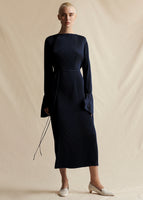 A model wearing a navy blue pleated midi length dress with a thin tie at waist.