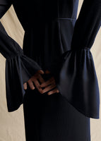 A close up of navy pleated dress with model's hands showing the flounce cuff.
