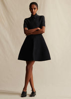 A model standing forwards wearing a black short sleeved mini dress.