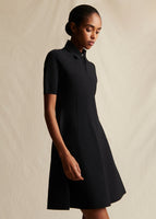 Model standing sideways wearing a black short sleeved mini dress.