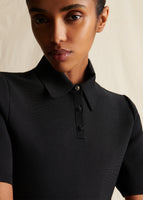 A close-up image of a model wearing a black short sleeved dress that has a collar and three buttons at neckline. Top button is crystal.